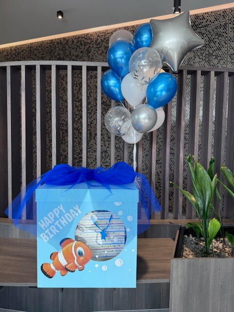 Nemo Birthday Box with Balloons Nemo-themed birthday gift box with blue tulle and a bunch of blue, silver and white helium balloons. "Happy Birthday" message on the front.